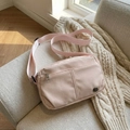 Light pink nylon crossbody bag with adjustable wide strap on a soft grey sofa - Pink