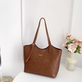 Braune Shopper-Tasche aus Leder mit langen Griffen und goldenem Schriftzug auf weißem Tisch - Braun (Ohne Anhänger)