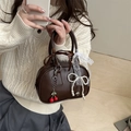 Deep brown leather handbag with pearl bow and cherry pendant shown in hand - Brown