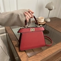 Chic red textured leather trapezoid handbag with gold rotating lock on wooden table - Red