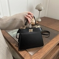 Elegant black leather trapezoid handbag with gold twist lock in a cozy desk setting - Black
