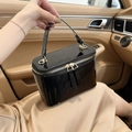 Glossy black patent leather box bag with gold zippers on luxury car seat background - Black