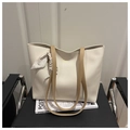Detail of cream tote bag with gold logo and patterned silk scarf on a black seat - White