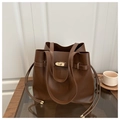Detail of a dark brown leather bucket bag with a golden twist lock on a wooden table - Coffee