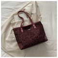 Close-up of leopard print tote bag with burgundy leather trim and golden metal rivets - Red