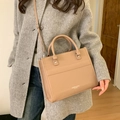 Detail of light brown leather tote bag with embossed text worn with a grey wool coat - Khaki