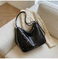 Close-up of black glossy leather hobo bag with side zipper and elegant brand logo - Black