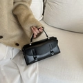 Bolso de mano cuadrado de cuero negro minimalista con costuras paralelas sostenido por una modelo - Negro