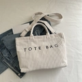 White corduroy tote bag with black embroidery and adjustable strap in lifestyle setting - White