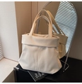 Detalle de un bolso tote blanco crema con costuras verticales y asas anchas en una mesa - Blanco