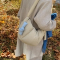 Borsa a tracolla imbottita color crema con fiocco blu indossata da modella in parco autunnale - Cachi