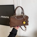 Brown suede Boston handbag with bow detail and fur pompom charm held by hand - Coffee With Pendant