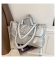 Detail of silver metallic puffer tote bag with quilted texture on a white suitcase - Silver