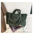 Detail of dark green quilted puffer tote bag with glossy texture on white luggage - Green