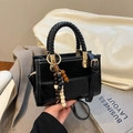 Black leather handbag with woven handle and wooden bead tassel in a stylish textured finish - Black