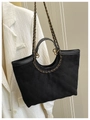 Detail of black quilted tote bag with chain strap against a white blazer - Black