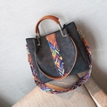 Sac cabas gris foncé en daim avec bandoulière tissée arc-en-ciel posé sur un canapé beige - Noir