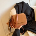 Brown rectangular crossbody bag with leather patchwork and tassel detail shown on a chair - Small / Brown