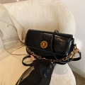 Classic black oil wax leather crossbody bag with gold chain and twist lock on a white chair - Black