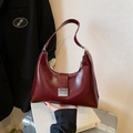 Bolso hobo chic en cuero brillante burdeos con hebilla de metal plateado sobre un libro - Rojo