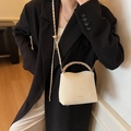 Elegante beige gesteppte Kettentasche mit Lederriemen auf einem dunklen Blazer - Weiß