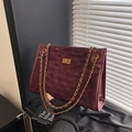 Elegante bolso tote acolchado color vino con cadena dorada y cierre metálico bajo luz natural - Rojo