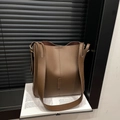 Braune Leder-Eimertasche mit weißen Ziernähten auf einem Buch in künstlerischer Umgebung - Braun