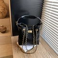 Schwarze Stepp-Eimertasche mit Goldschloss und Kette auf sonnigem Holztisch - Schwarz