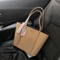 Detail of khaki tote bag with textured leather and decorative scarf on car seat - Brown