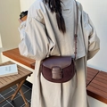 Dark brown saddle bag with contrast stitching and leather strap on a wooden bench - Brown