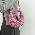 Schillernde gewebte Handtasche mit Knotendesign an einem Model vor grauer Wand - Rosa