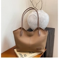 Detail of caramel leather tote bag with embossed label on a minimalist wooden background - Brown