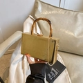 Goldene Box-Tasche mit Bambusgriff und Kettengurt vor einem beigen Hintergrund präsentiert - Gold