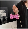 Metallic rose pink bow-shaped evening clutch bag with gold chain strap held by model - Pink
