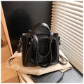 Detail of black crocodile texture handbag placed on a beige blazer with a vintage prop book - Black