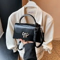 Chic black trapezoid handbag with a silver bow clasp and adjustable crossbody strap - Black
