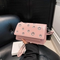 Pink minimalist crossbody bag with silver eyelets and a flap top, handheld showing - Pink