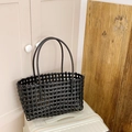 Minimalist black hollow woven tote bag displayed on white luggage in home setting - Black