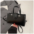Detail of a black crossbody square bag with silver hardware on a neutral fabric backdrop - Black