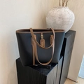 Minimalist black pebbled leather tote bag with brown trim on a rustic display stand - Black
