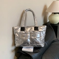 Metallic silver quilted puffer tote bag with black handles on a black leather sofa - Silver