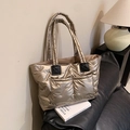 Champagne gold quilted puffer tote bag with large front pockets on a black sofa - Champagne