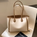 Elegante bolso tote crema con ribete marrón y asas dobles sobre una silla moderna - Blanco