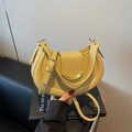 Light yellow textured leather crescent shoulder bag with gold metal buckle on a book - Yellow