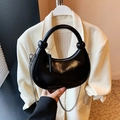 Glossy black hobo bag with silver chain and knotted handle in a stylish outfit context - Black