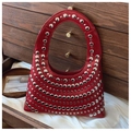 Détail d'un sac cabas en cuir rouge foncé avec rivets métalliques sur fond de bois sombre - Rouge