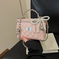 Détail d'un sac matelassé rose avec nœud en perle et breloque cœur sur un fond de cuir - Rose