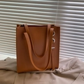 Bolso tote de cuero marrón con ojales metálicos y hebilla sobre fondo de traje elegante - Marrón