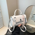 White faux leather crossbody bag with woven charm and silver clasp in lifestyle setting - White (With Charm)