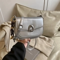 Minimalist silver saddle bag with metallic finish and woven charm shown in hand - Silver with Charm
